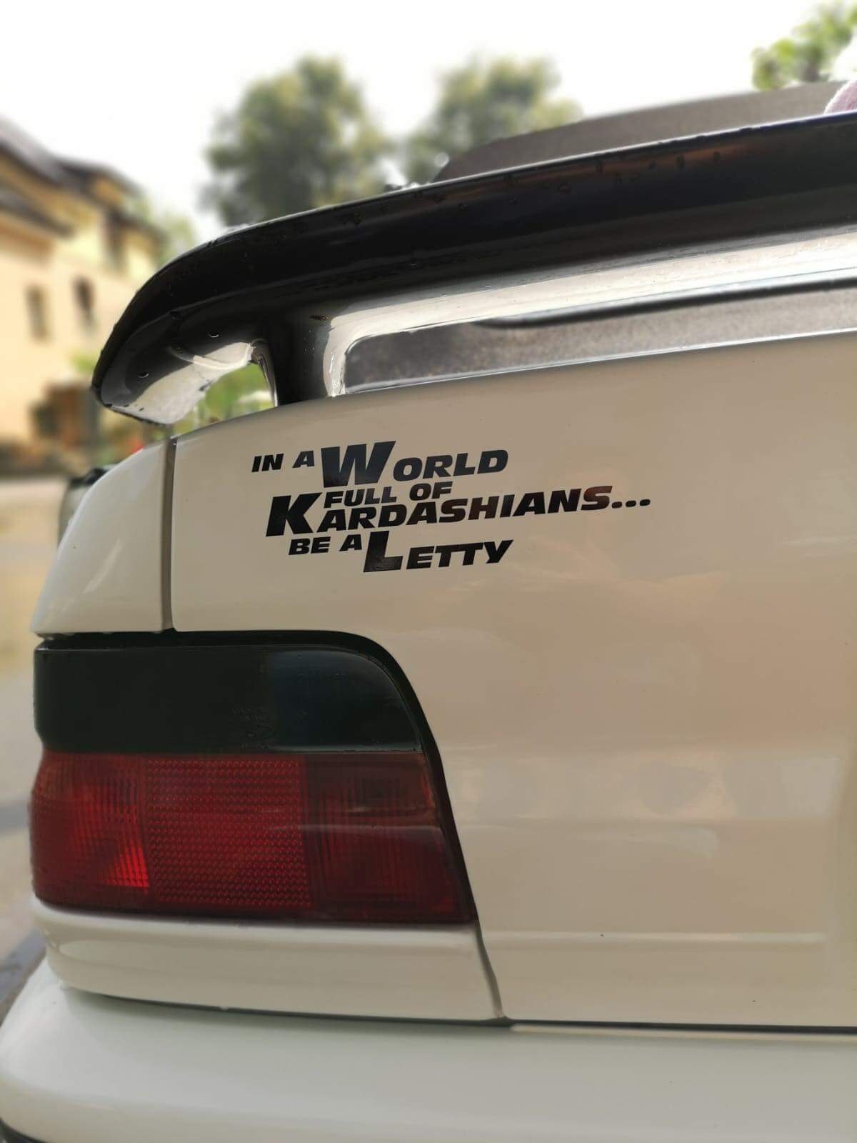 Schwarzer Letty Aufkleber mit dem Spruch „In a World full of Kardashians… be a Letty“ am Heck eines weißen Autos mit Spoiler