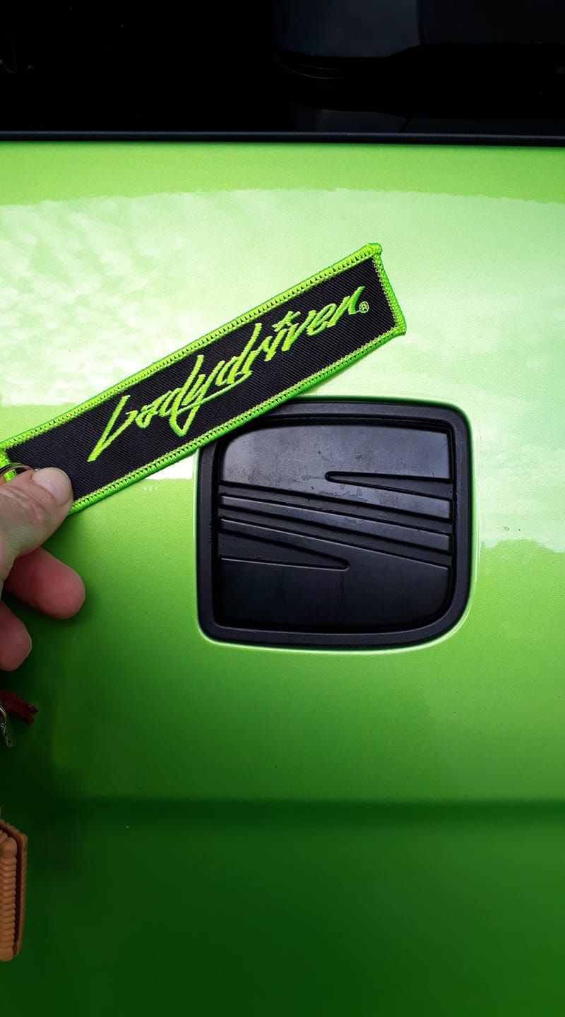 Grüner Ladydriven Schlüsselanhänger mit gesticktem Logo vor einem grünen Fahrzeug