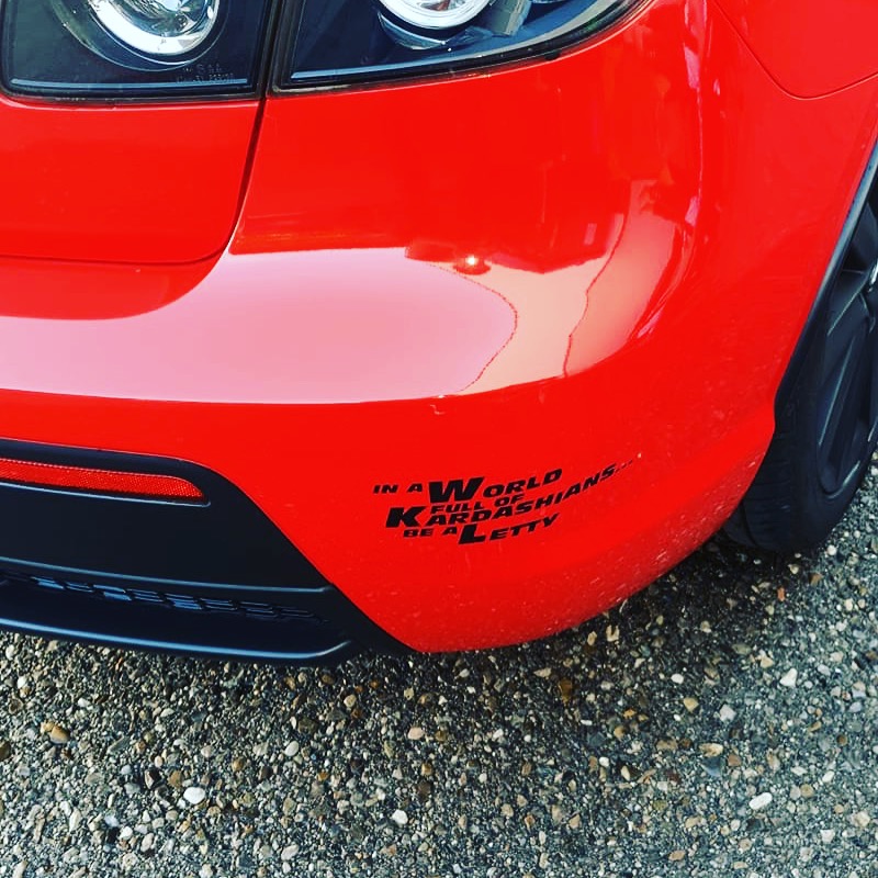 Schwarzer Letty Aufkleber mit dem Spruch „In a World full of Kardashians… be a Letty“ am Heck eines roten Autos
