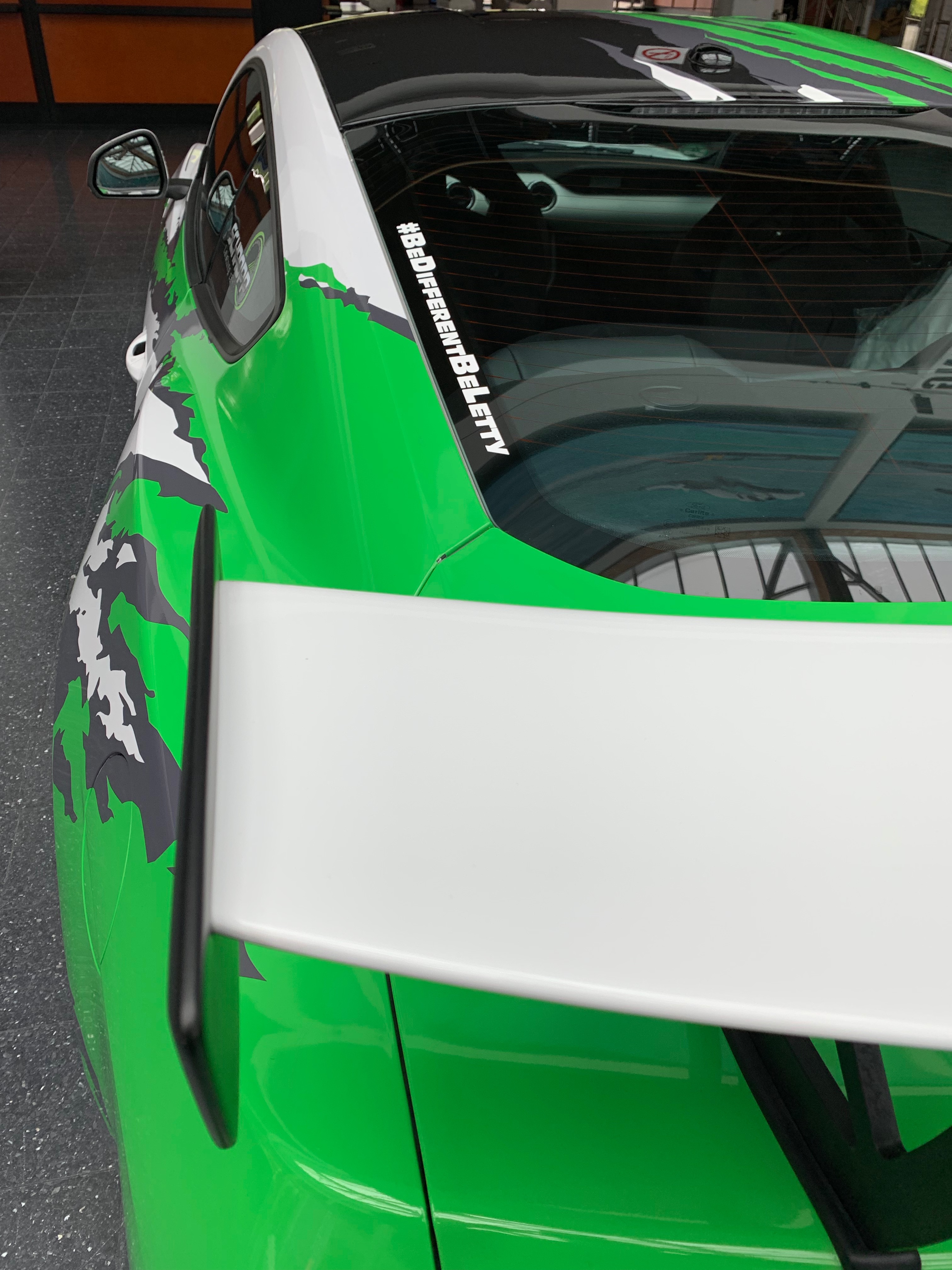 Weißer #BeDifferentBeLetty Aufkleber auf der Heckscheibe eines grünen Autos